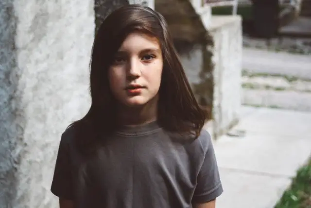 Close-up of a young long-haired boy standing outside and looking seriously at the camera.