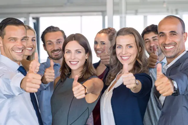 Group of happy businesspeople showing a sign of success. The successful business team showing a thumbs-up sign and looking at the camera. Smiling businessmen and businesswomen cheering at the office.